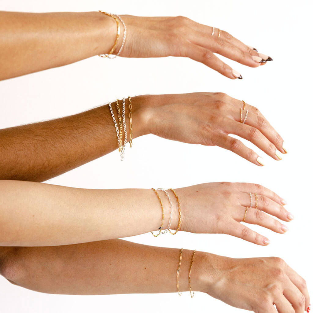 Multiple hands showcasing an array of Everlinx permanent jewelry bracelets in different designs and colors.